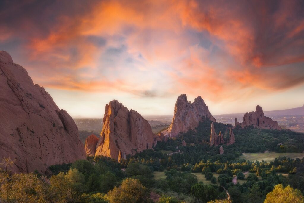 Sunset over orange rock formations of Garden of the Gods, with green trees and a distant valley beneath the dramatic sky C5.a (informative)