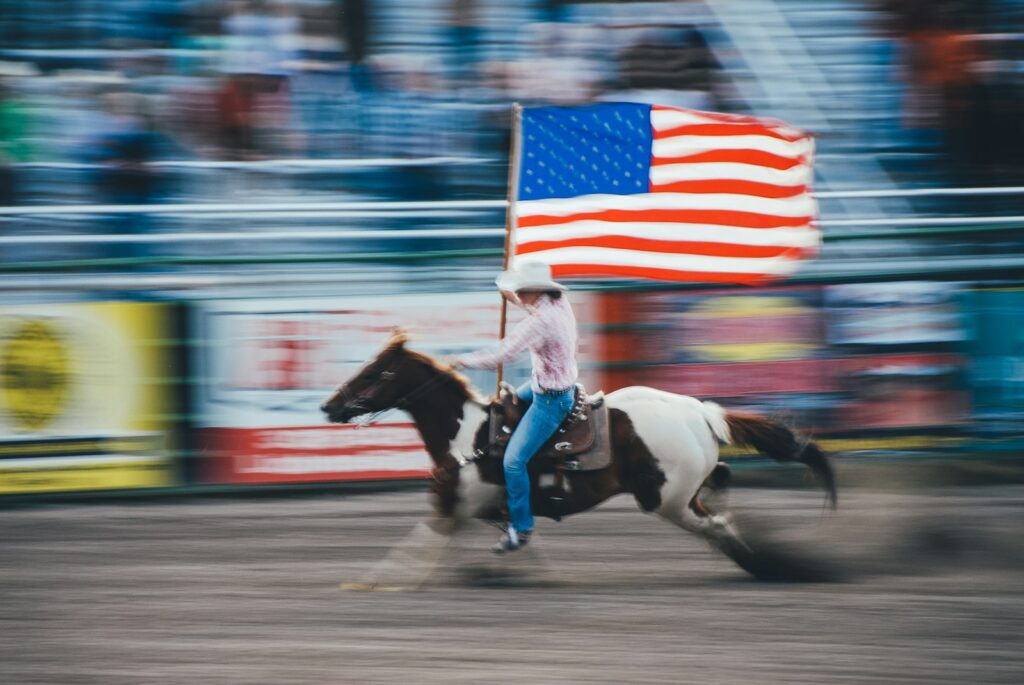 Photo by Melissa Walsh - Colorado Frontiers time lapse photo of man carrying U.S. flag while riding brown horse
